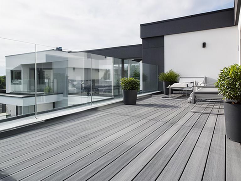 Pavimento de composite gris en una terraza exterior contemporánea con barandilla de vidrio
